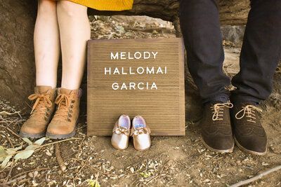 A man and a woman are sitting next to a letter board with a pair of baby shoes on it. Baby announcement. Maternity.