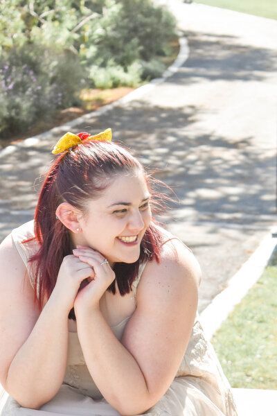 A woman with red hair and a yellow bow in her hair is smiling