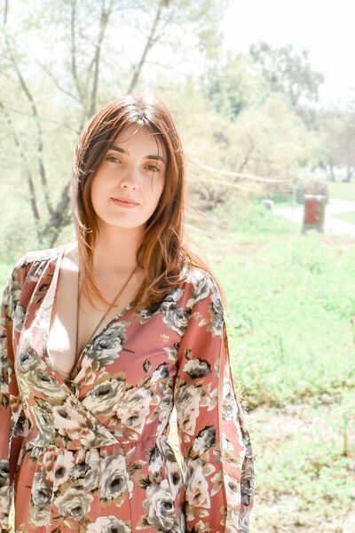 A woman in a floral dress is standing in a field.