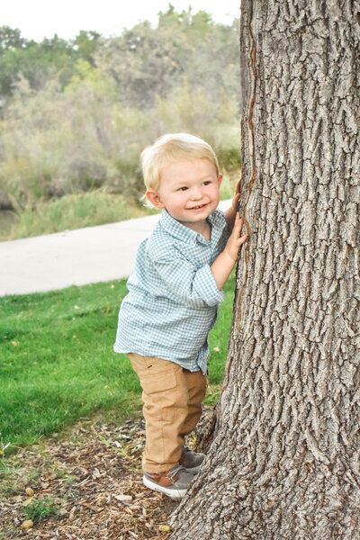 A little boy is standing next to a tree trunk.