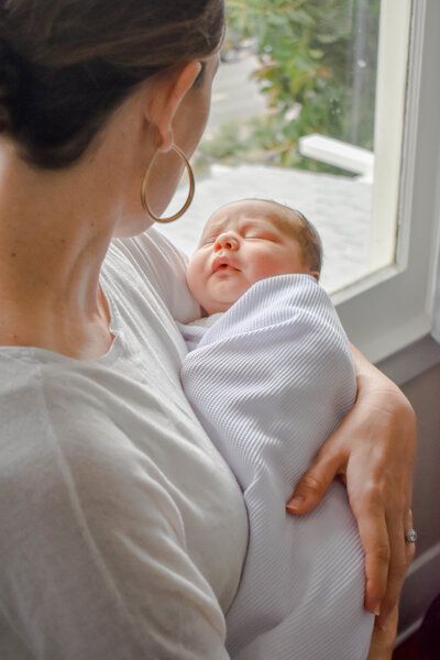 A woman is holding a newborn baby wrapped in a white blanket.