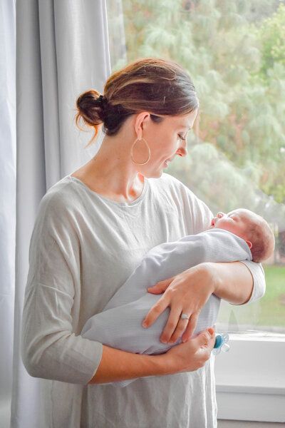 A woman is holding a newborn baby in her arms in front of a window.
