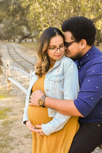 A man is hugging a pregnant woman in a park. Maternity,