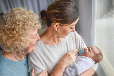 A woman is holding a baby in her arms while two women look on. Generational family photo.