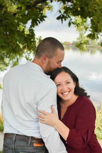 A man is kissing a woman on the cheek in front of a lake.