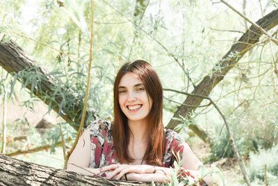 A woman is leaning against a tree trunk and smiling.