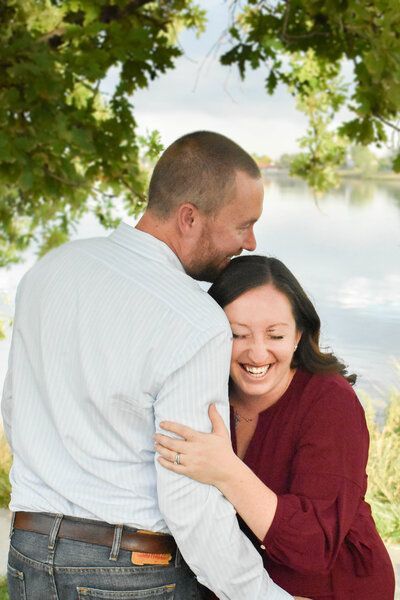 A man and a woman are hugging each other in front of a lake.