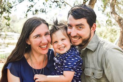 A man and woman are holding a child and smiling for a picture. Family.