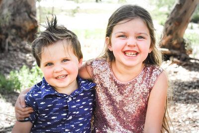A boy and a girl are sitting next to each other and smiling for the camera. Siblings. 
