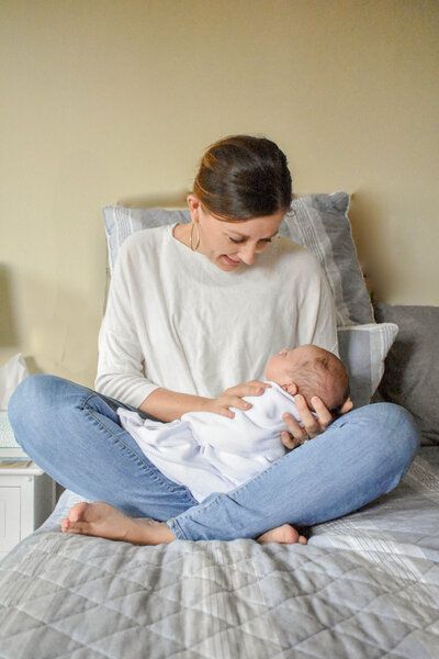 A woman is sitting on a bed holding a newborn baby. in home lifestyle session