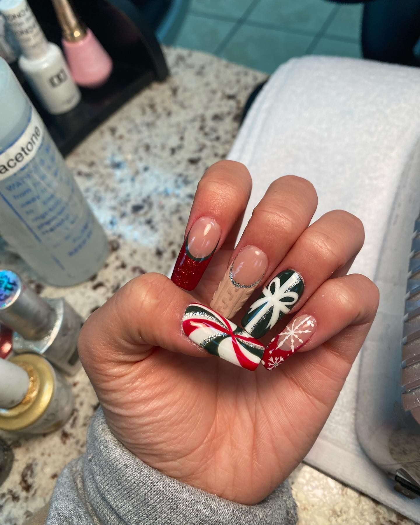 Hand with long nails featuring Christmas designs: red, white, and green candy cane, snowflakes, and French tips.