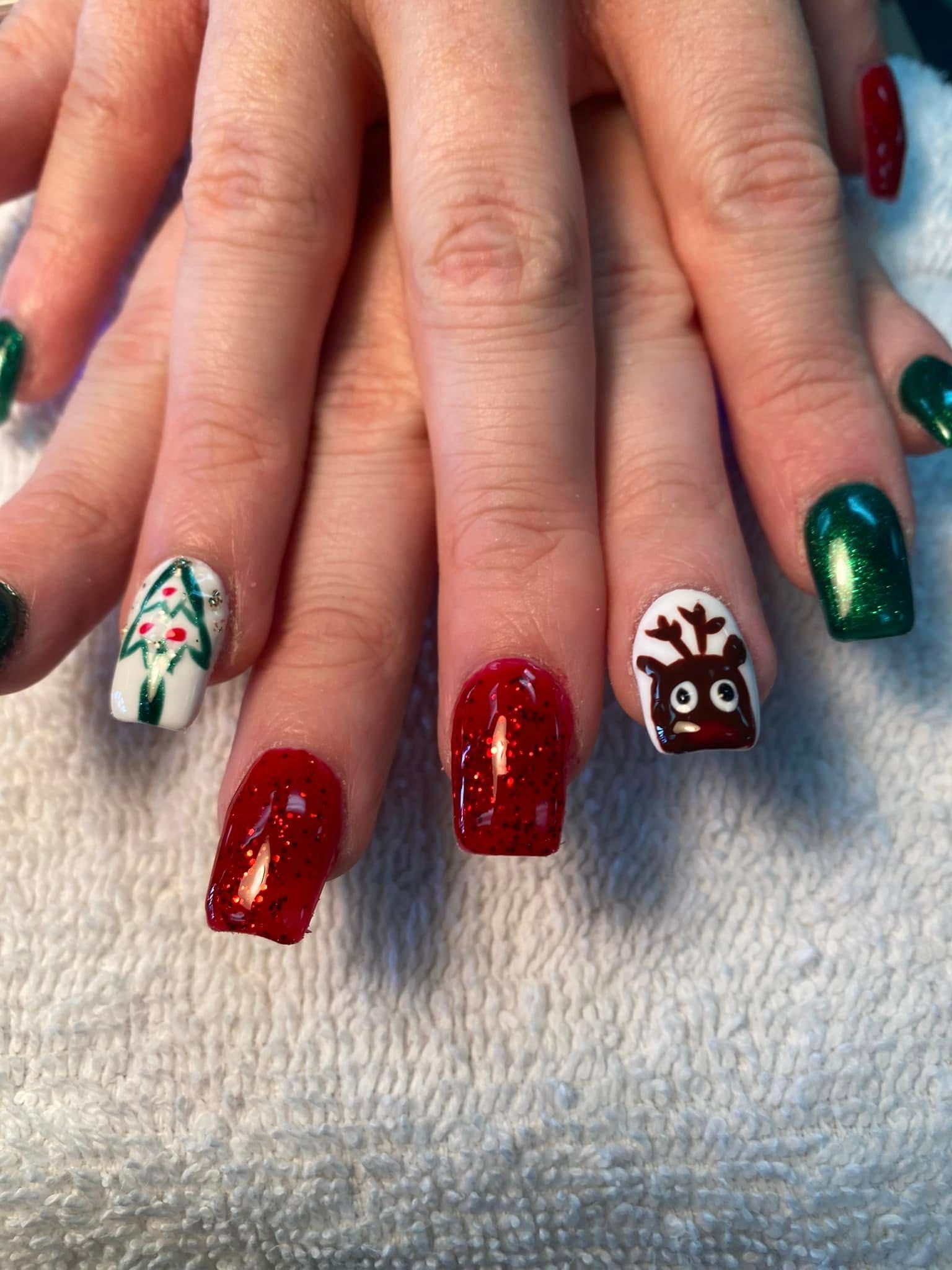 Christmas-themed nail art. Nails painted red, green, and white. Designs include a reindeer and a Christmas tree.