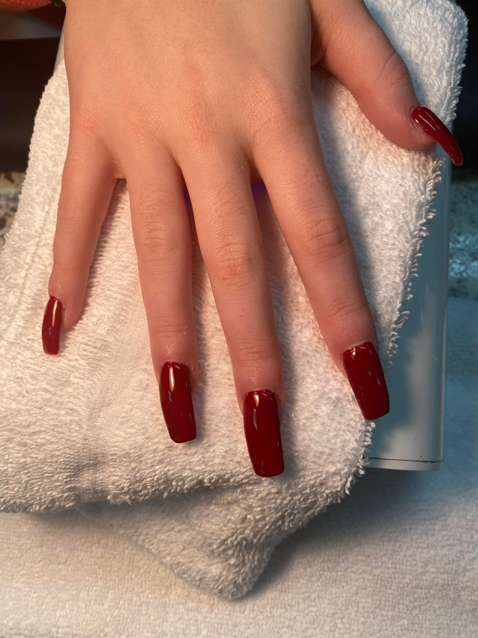 Hand with long, glossy, deep red rectangular fingernails resting on a white towel.