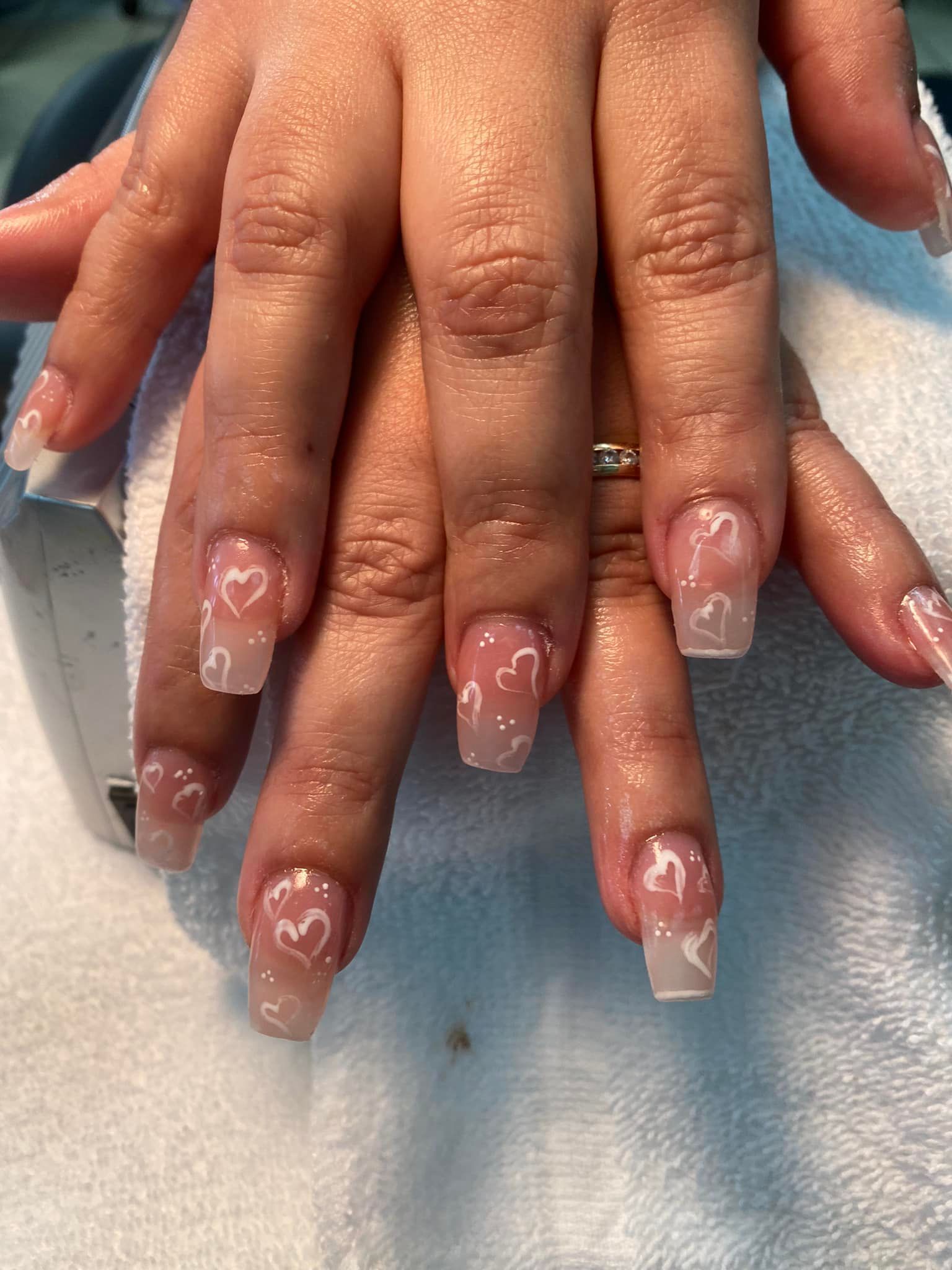 Hands with clear acrylic nails, white heart designs.