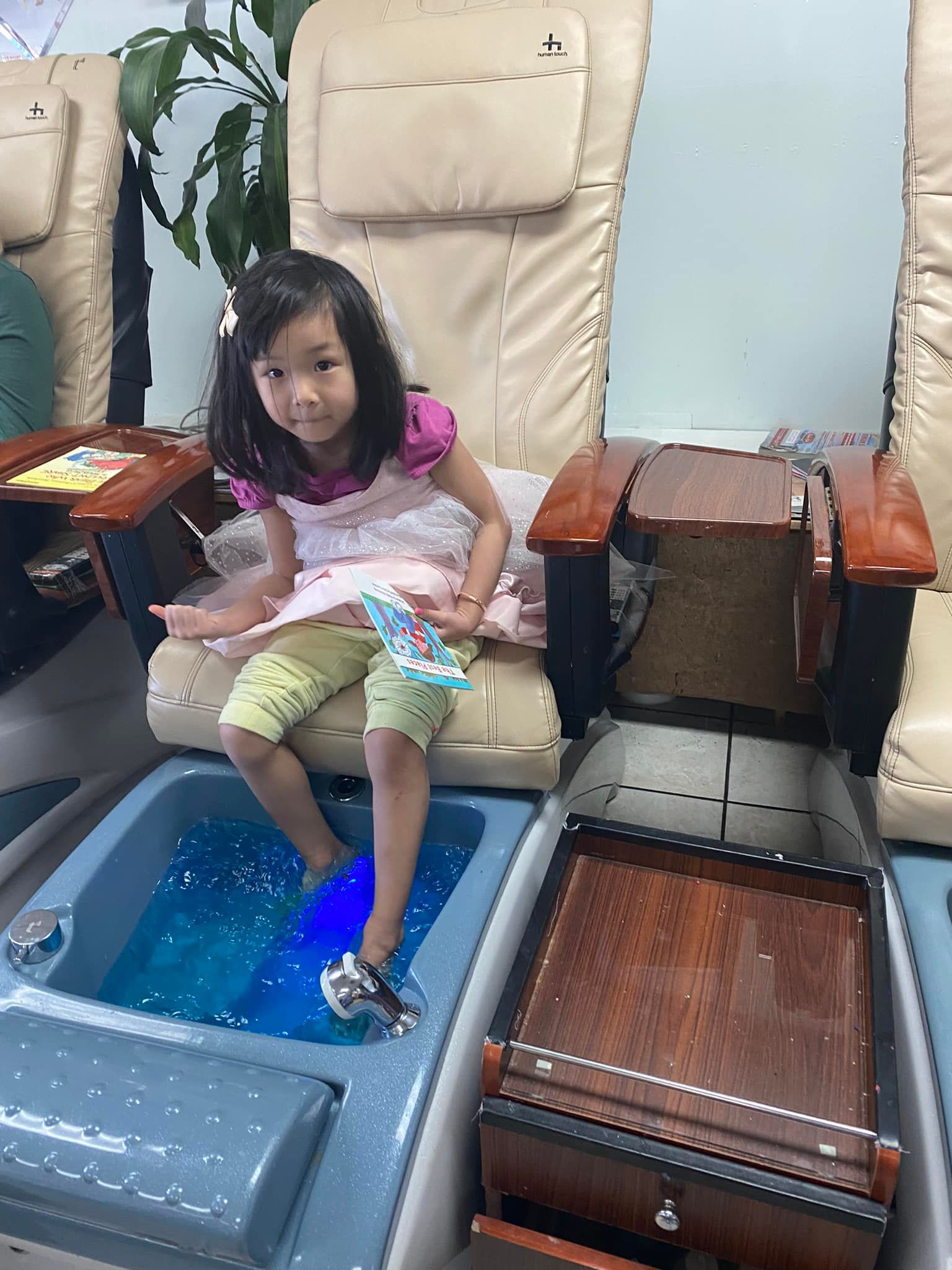 Young girl getting a pedicure in a salon, sitting in a massage chair, feet in blue water.