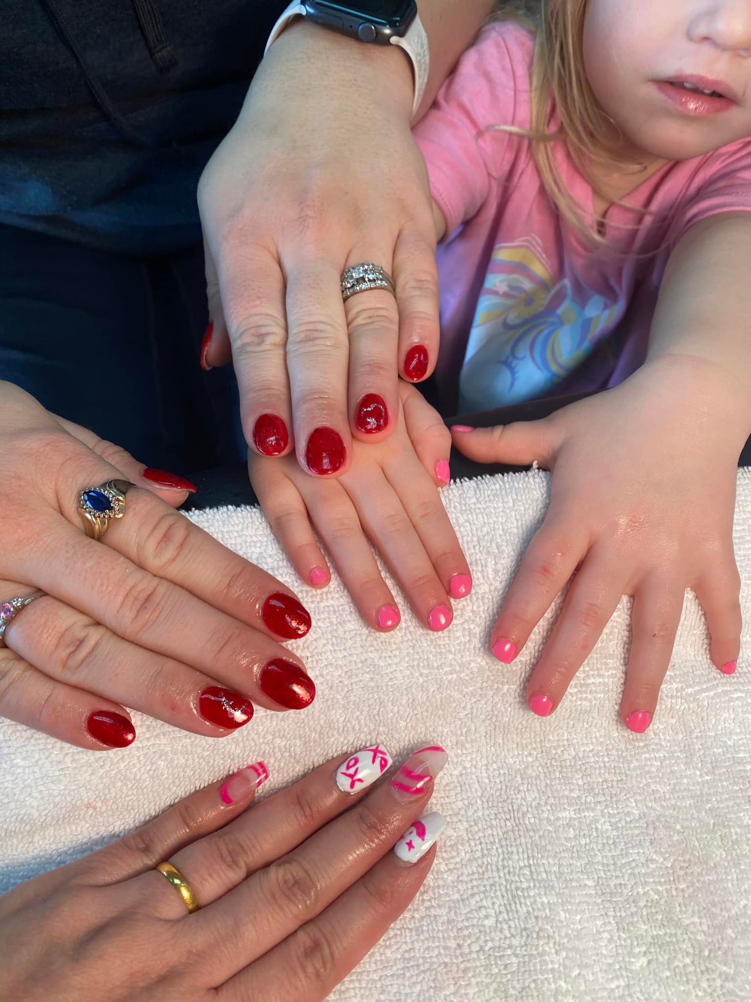 Four pairs of hands with manicured nails in shades of red and pink resting on a white towel.