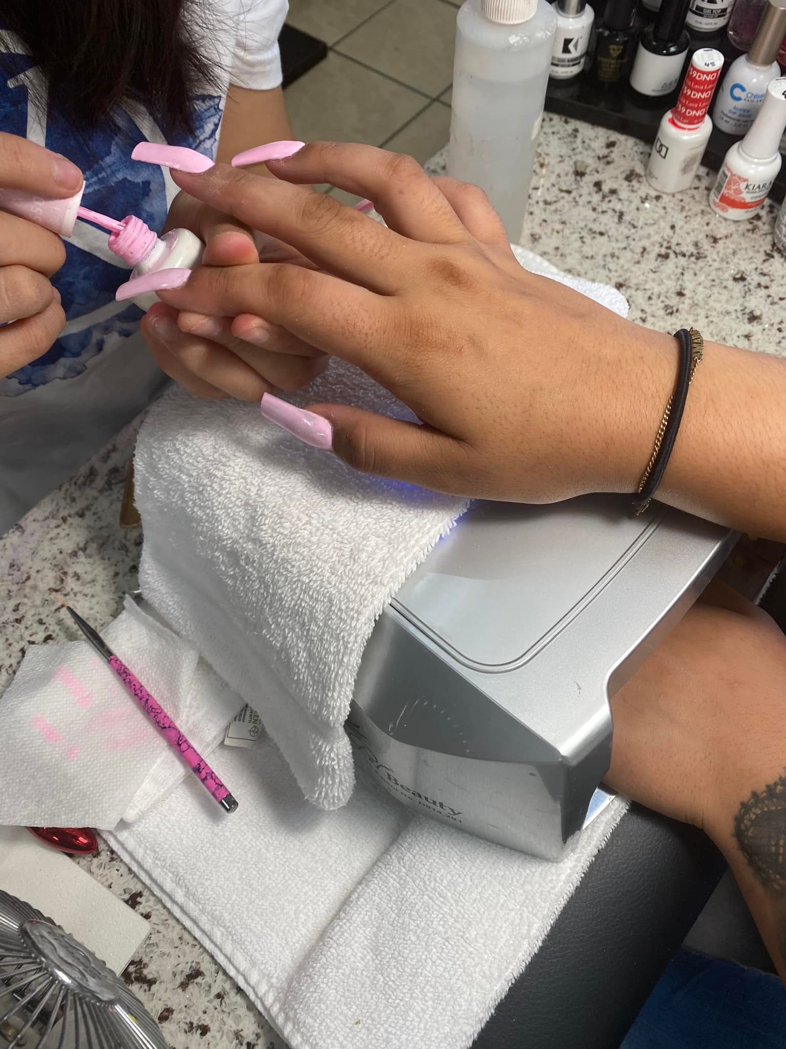 Person getting a manicure at a nail salon. A hand is being painted light pink, with a UV light and supplies visible.