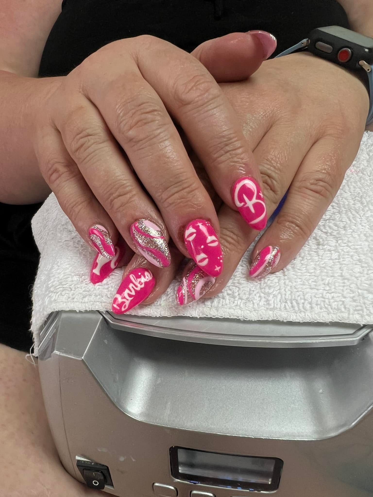 Hands with pink, decorated fingernails resting on a white towel over a silver machine.