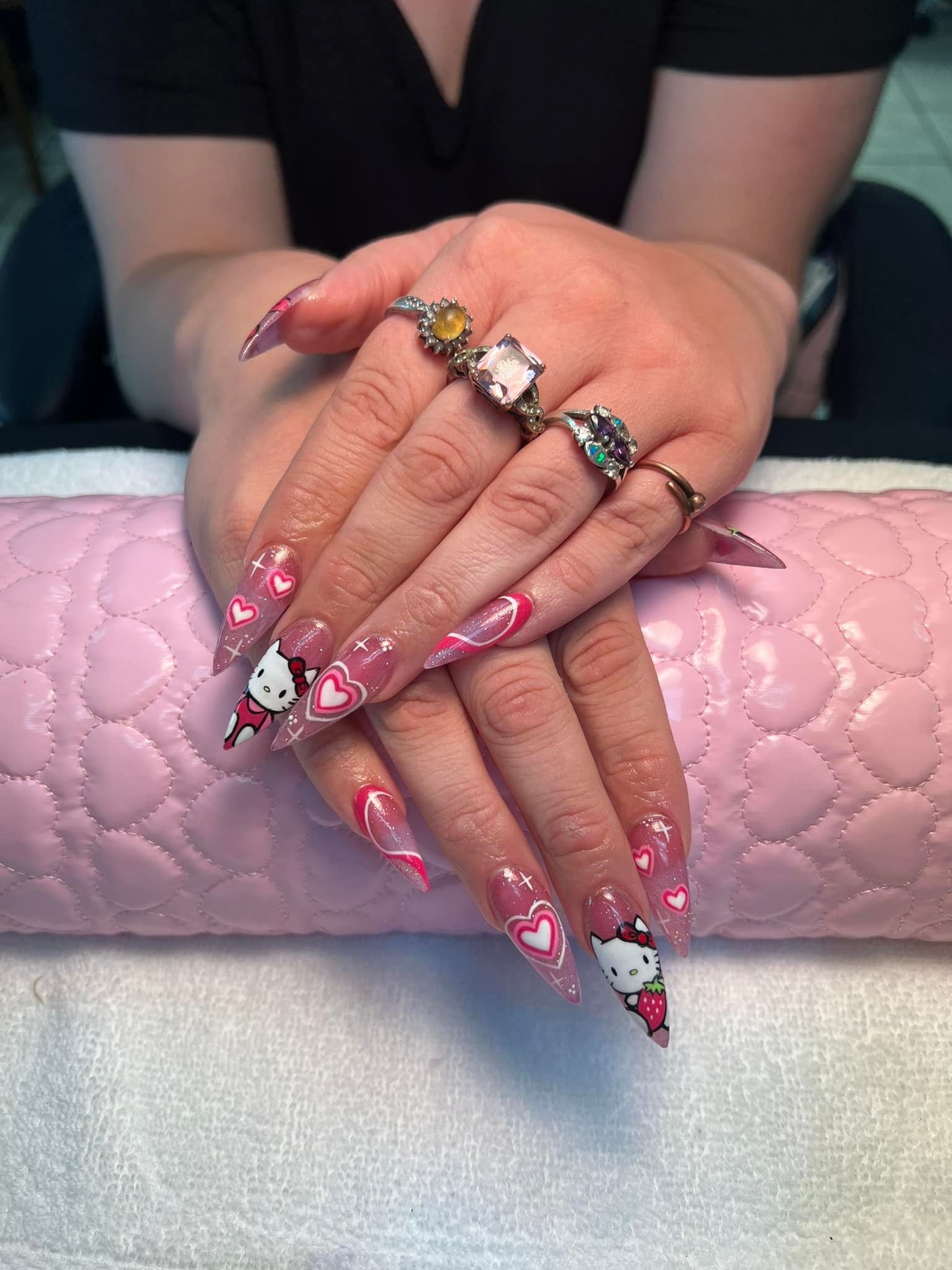 Long, pointed nails with Hello Kitty designs on pink manicure.
