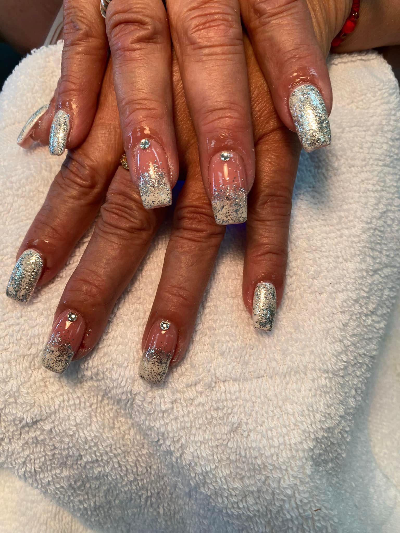 Hands with clear and sparkly glitter nail art, resting on a white towel.