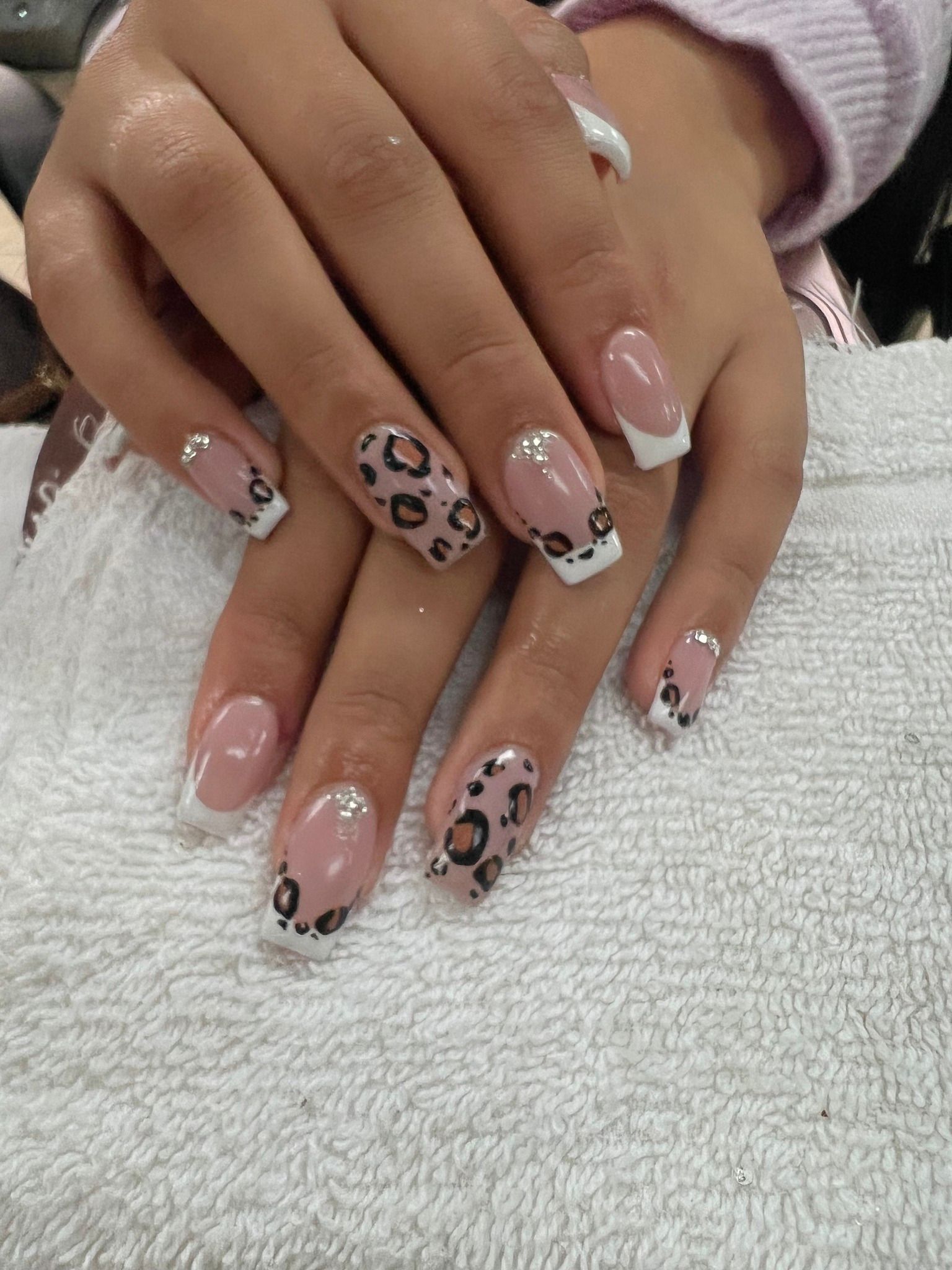 Hands with French manicure and leopard print nail art, resting on white towel.