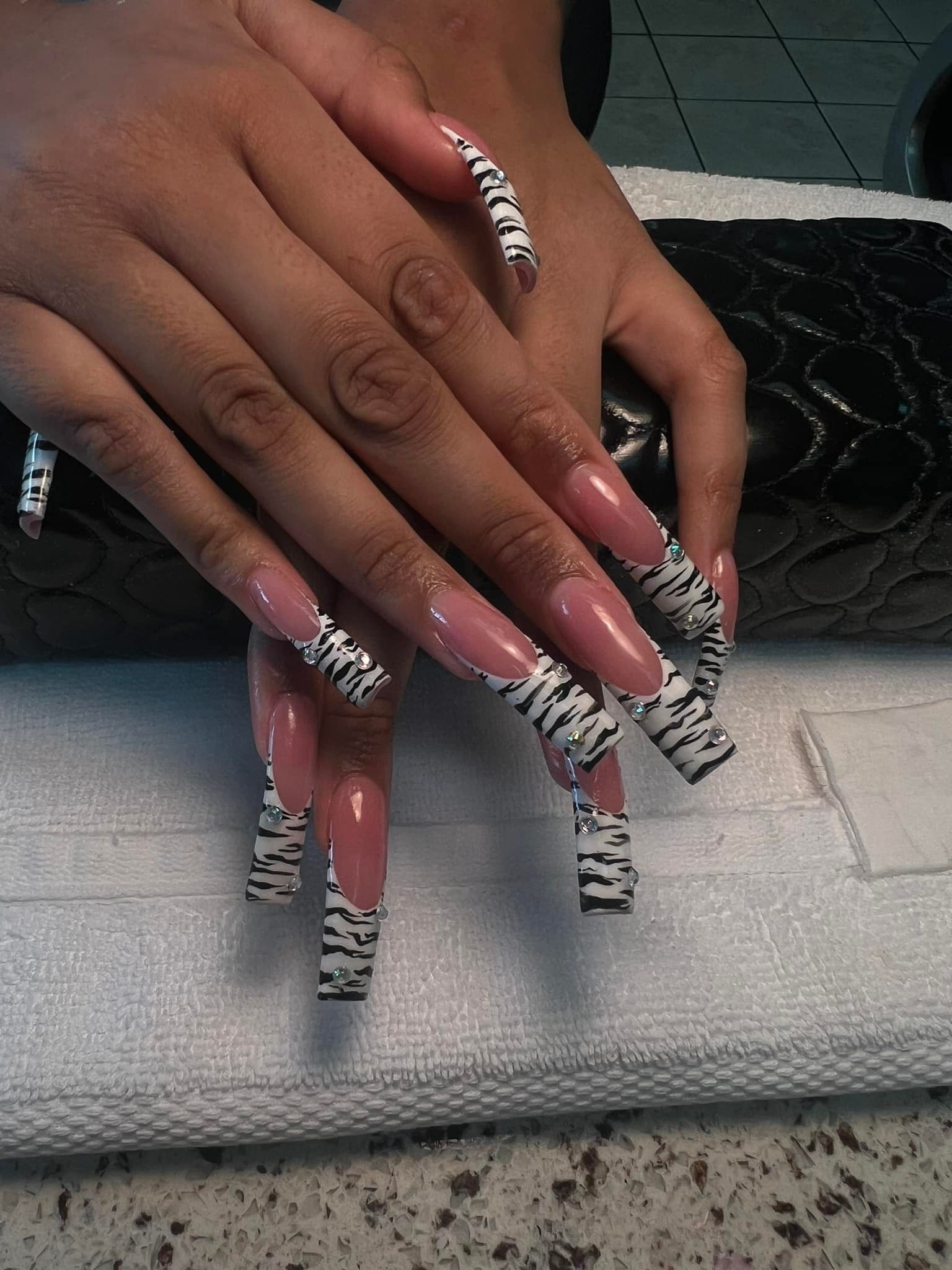 Long, patterned nails with zebra print and a pink French tip on a hand.