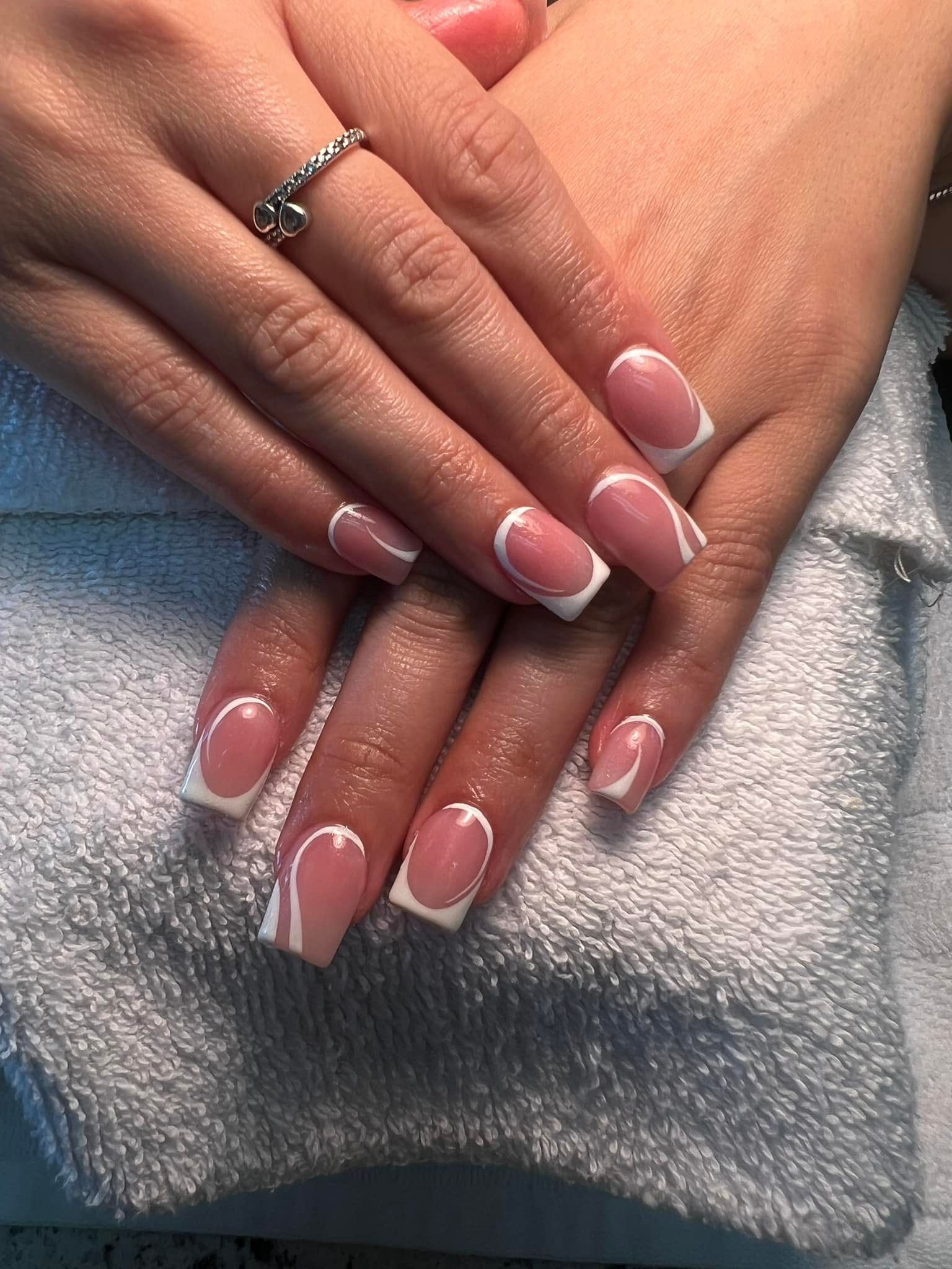 Hands with French tip square-shaped nails, wearing a silver ring, resting on a white towel.