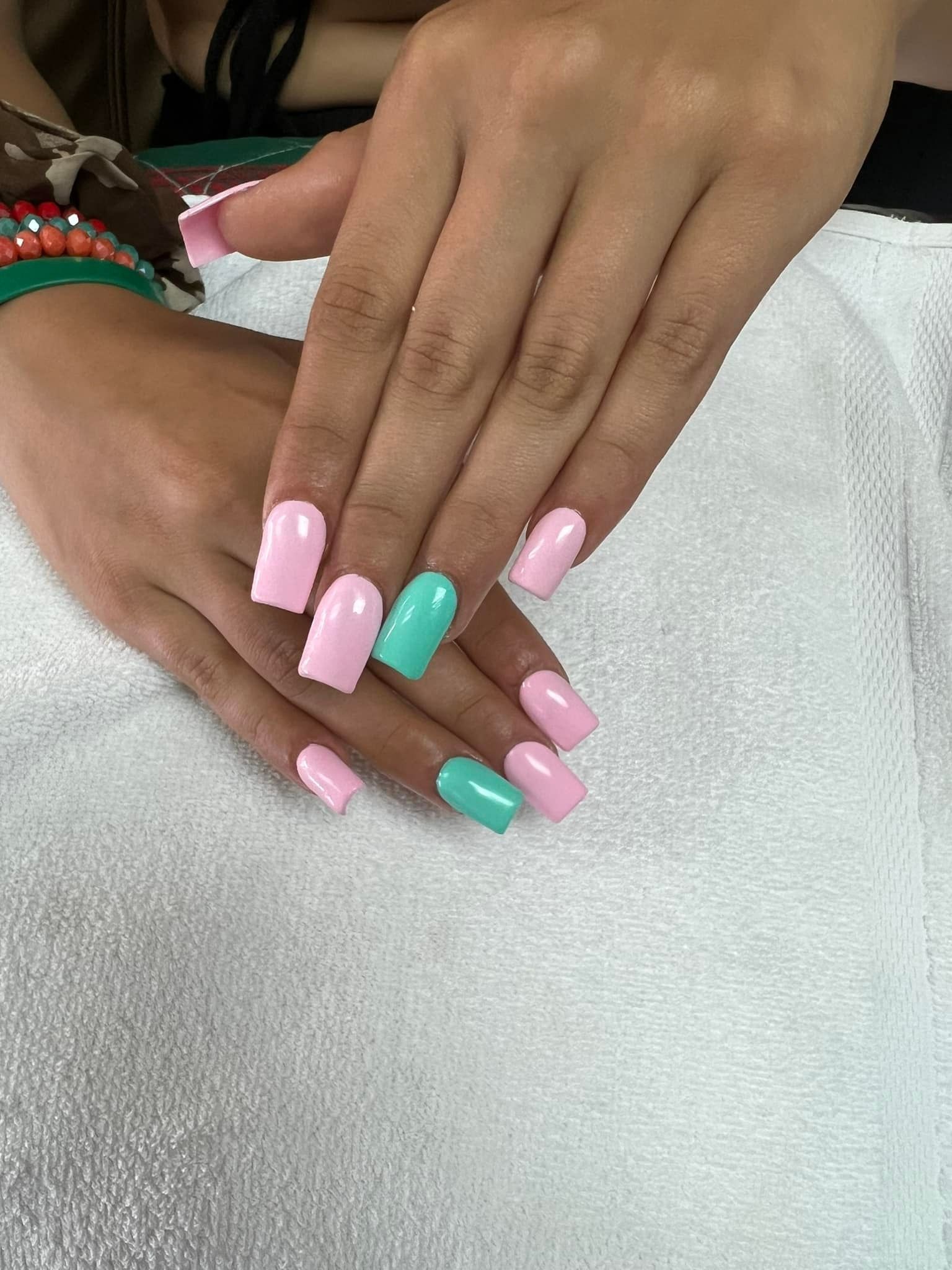 Hands with pink and teal square-shaped nails resting on a white towel.