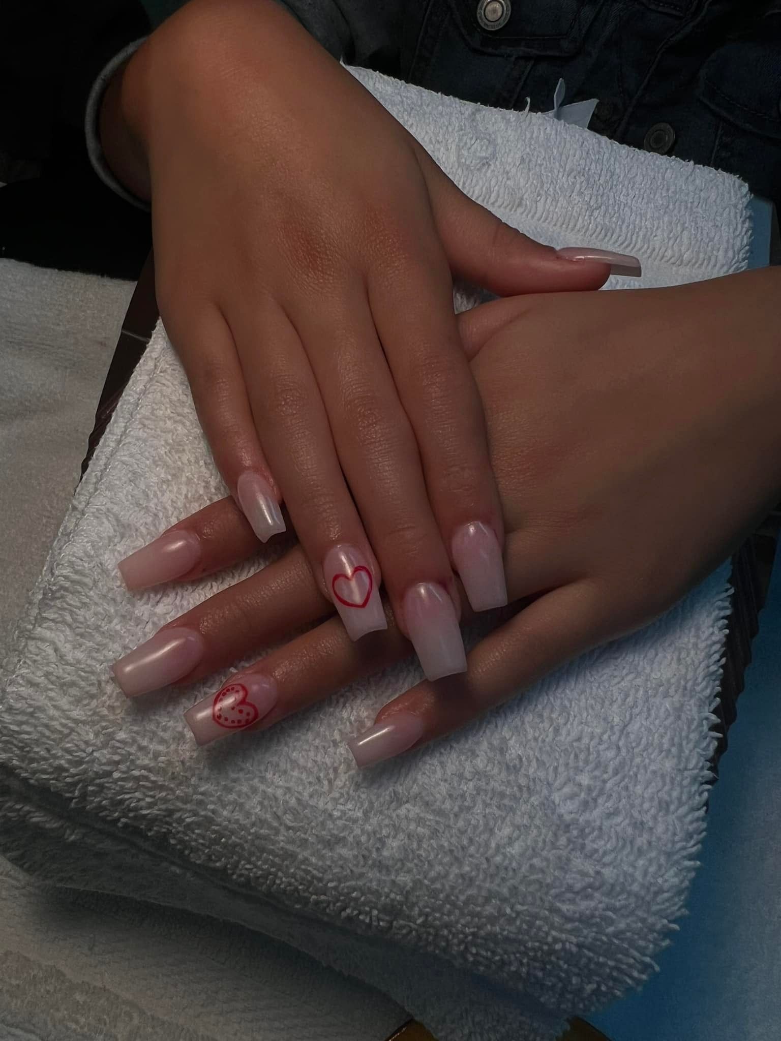 Hands with square acrylic nails, some with red heart designs, resting on a white towel.