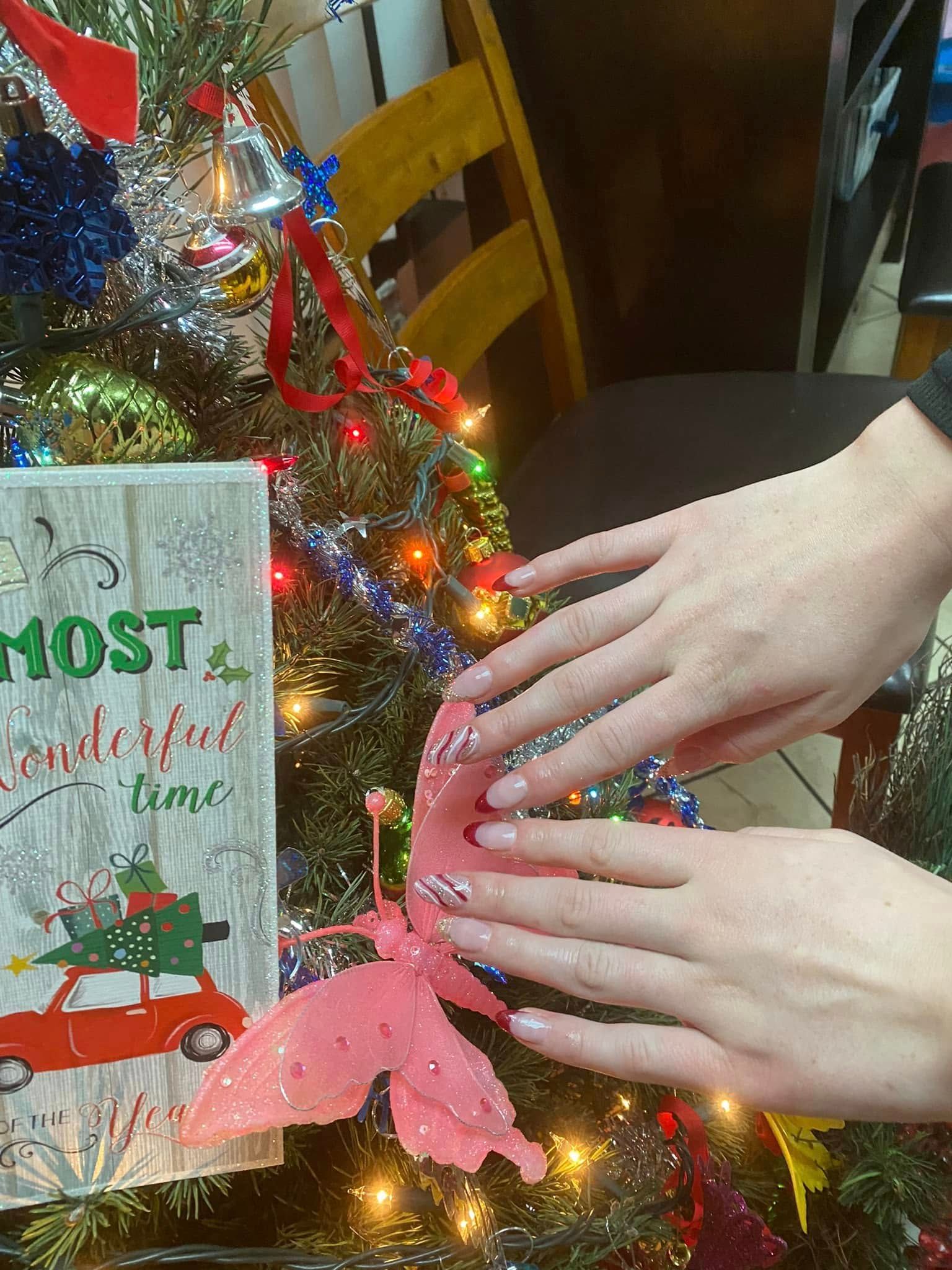 Hands with painted nails near a decorated Christmas tree with a 