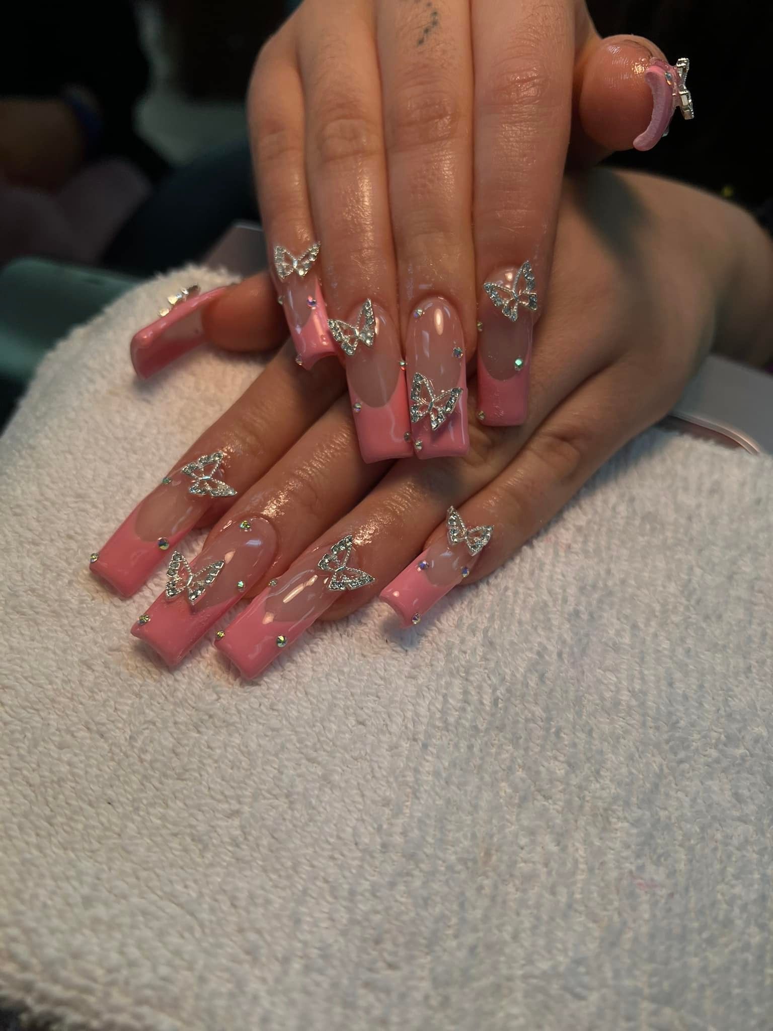Long pink and clear acrylic nails with silver butterfly embellishments.
