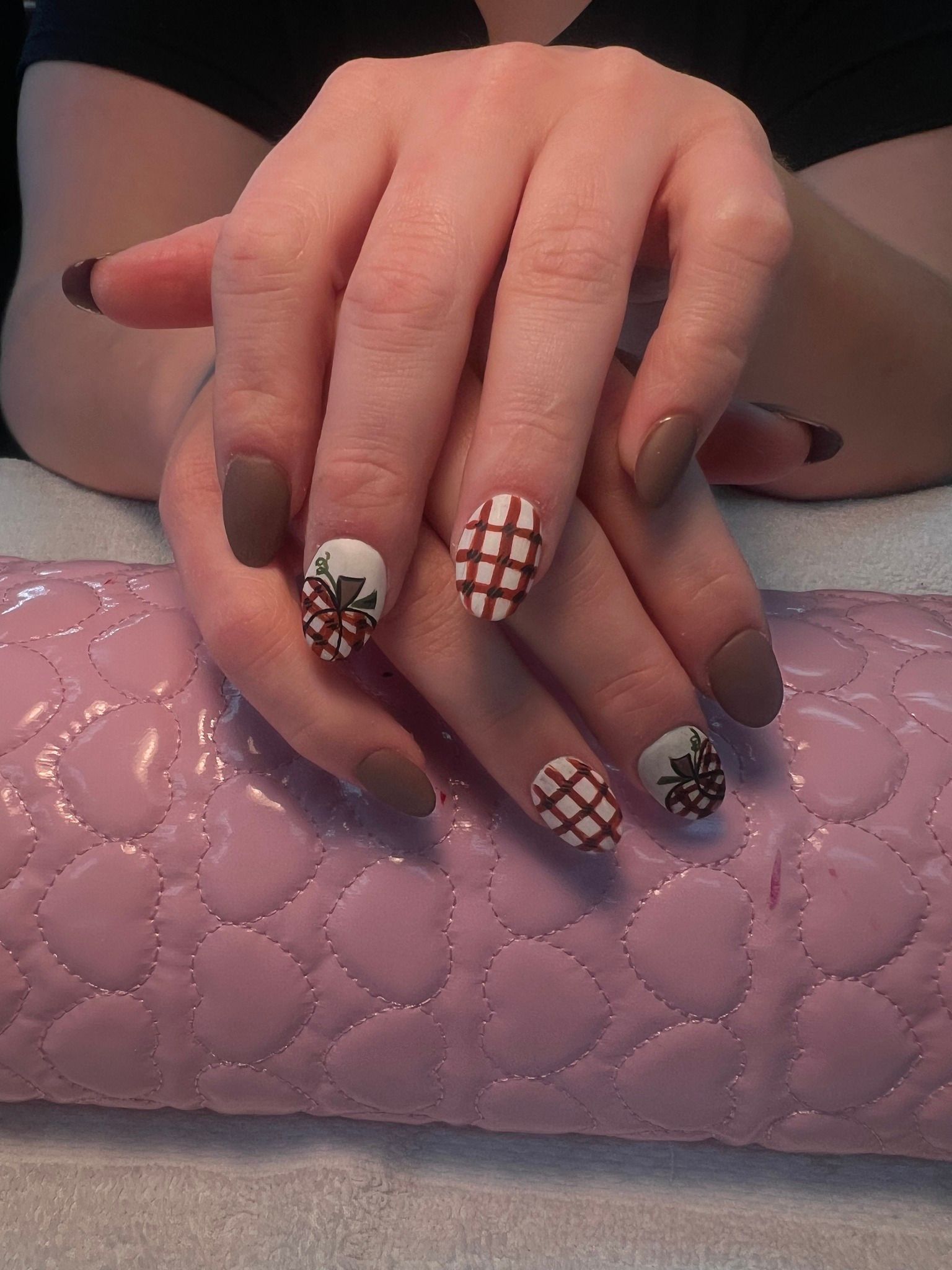 Hands with brown and white, grid-patterned nail art, resting on a pink cushion.