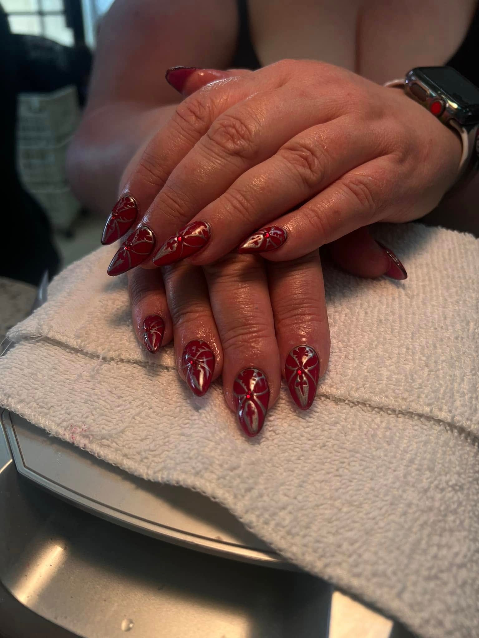 Hands with red stiletto nails decorated with intricate designs, resting on a white towel.