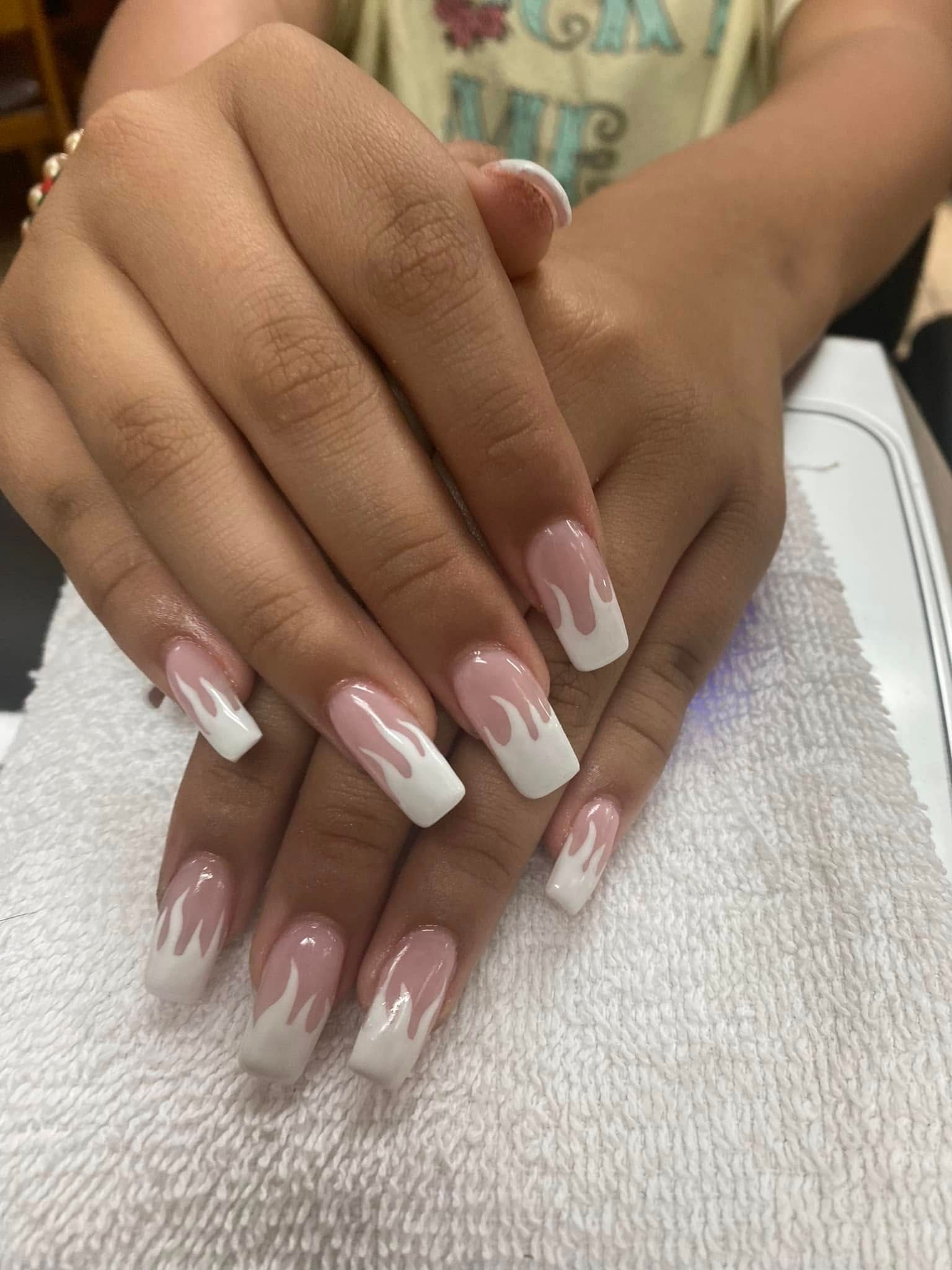 Hands with white flame-like nail art, resting on a white towel.
