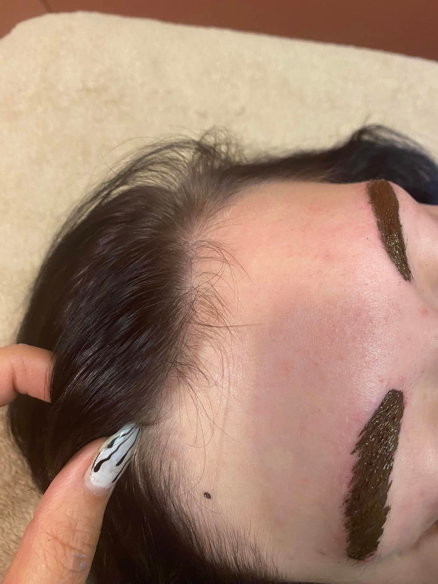 Person's forehead with henna dye on brows. Finger points to hairline, dark hair, and light skin.