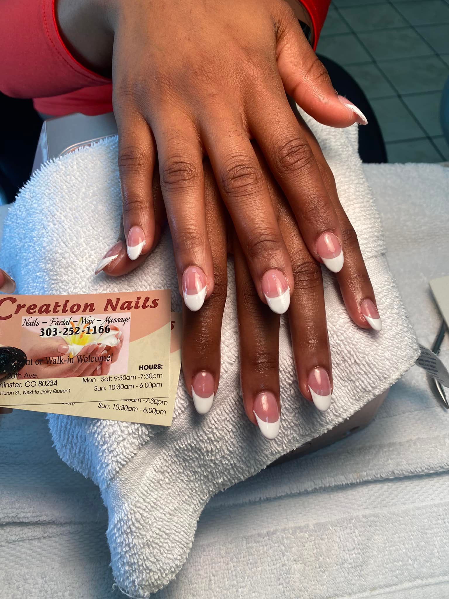 Hands with French tip nails, resting on a white towel, holding a business card for 