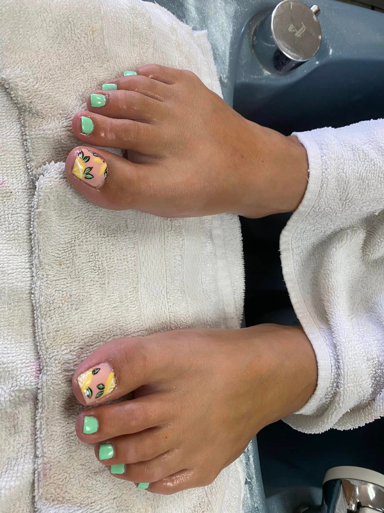 Feet with mint green toenails, one big toe with a yellow design, resting on a white towel.
