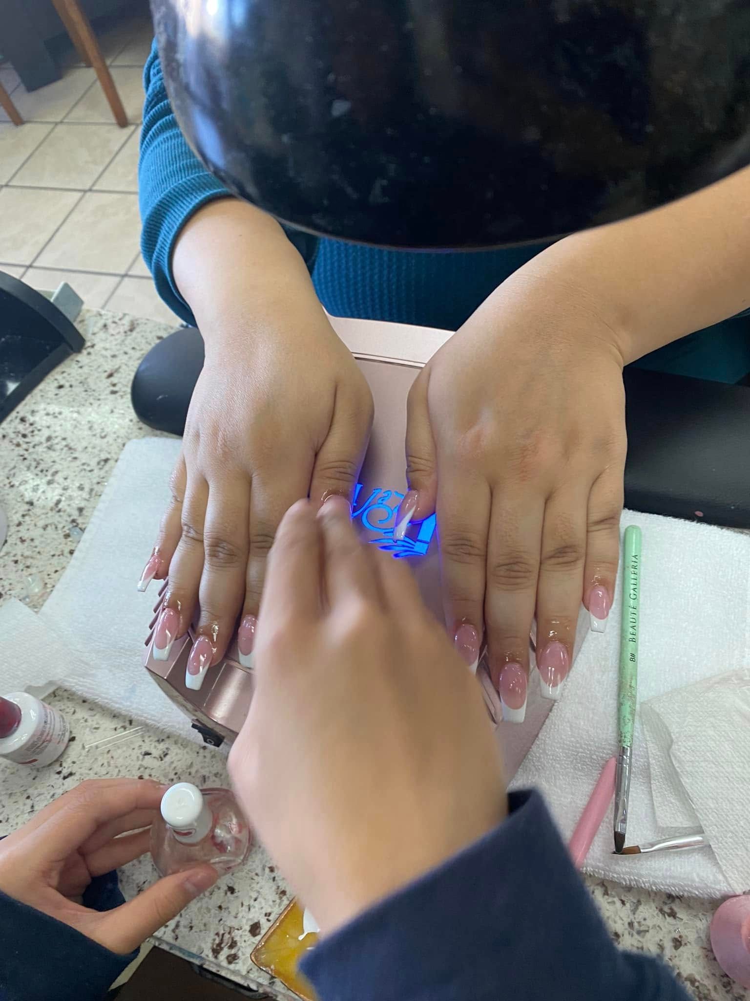 Hands getting a manicure with French tips under a UV light at a salon.