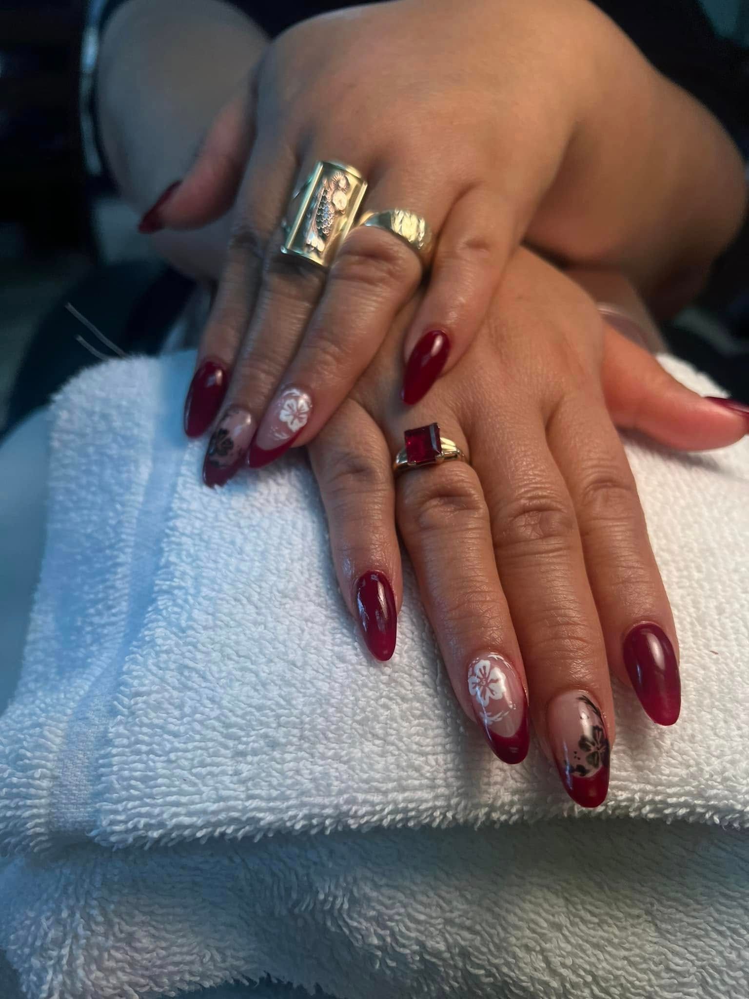 Hands with long, burgundy and nude colored nails with floral designs, adorned with rings on a white towel.
