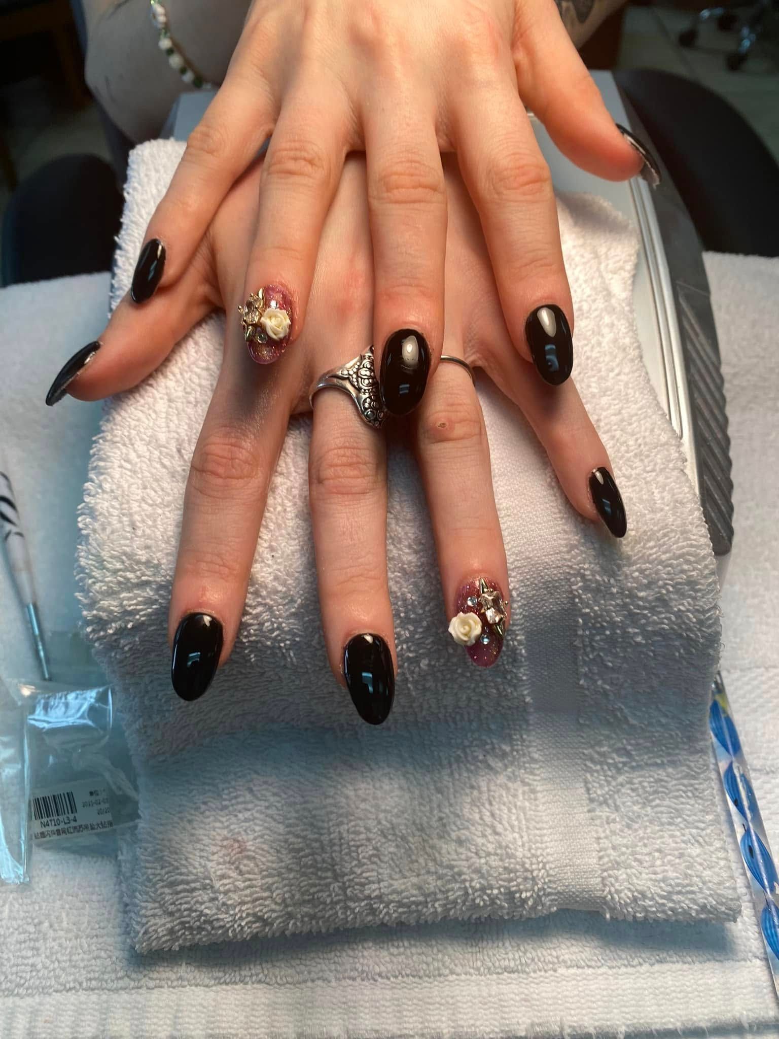 Hands with long, black, oval-shaped nails, some with floral and crystal designs. Resting on a white towel.