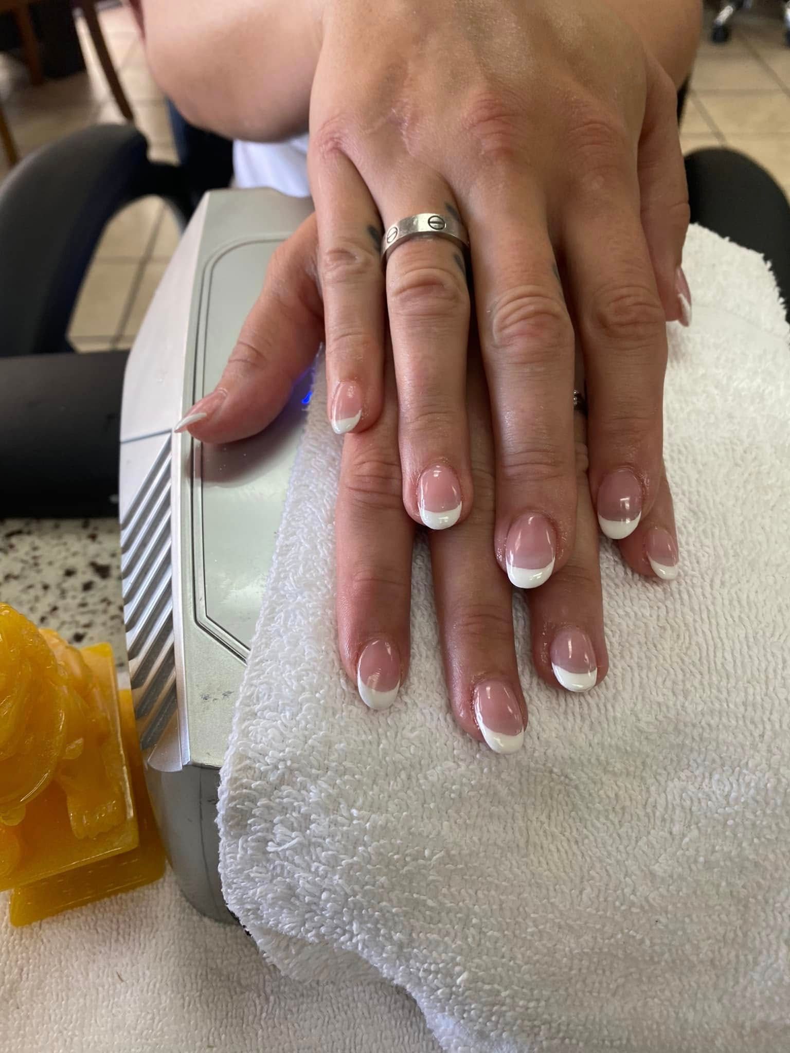 Person's hands with French tip manicure, resting on a white towel at a nail salon.