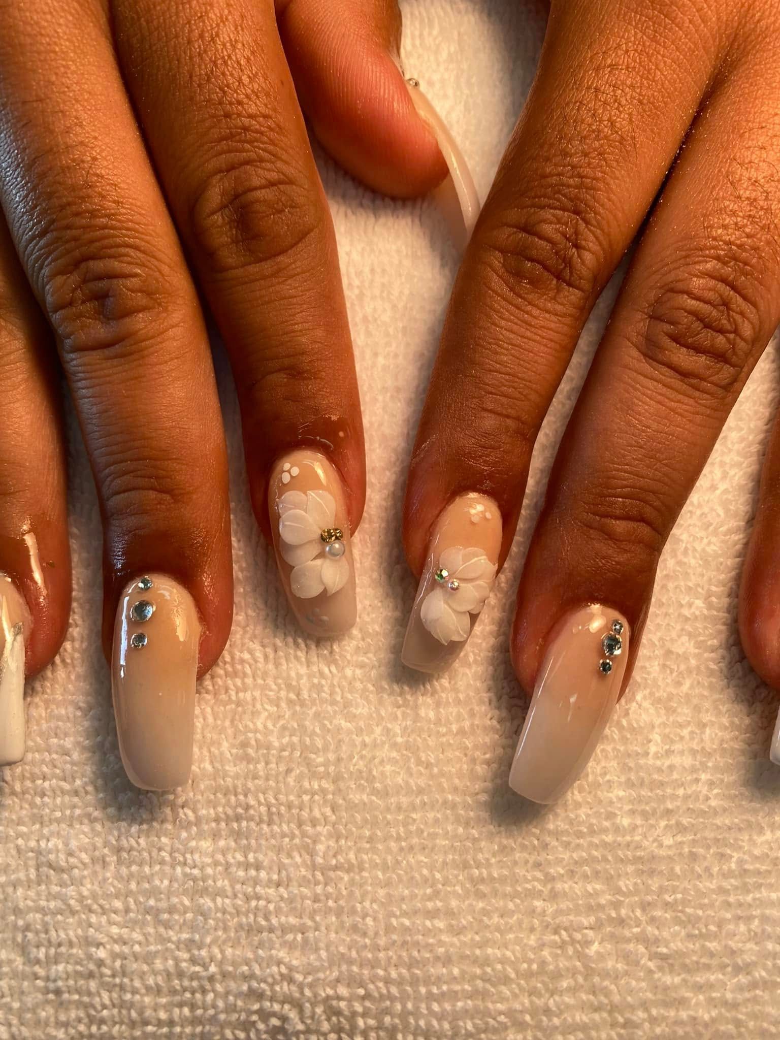 Manicured nails with white-to-beige gradient. Some nails feature white floral designs and rhinestones.
