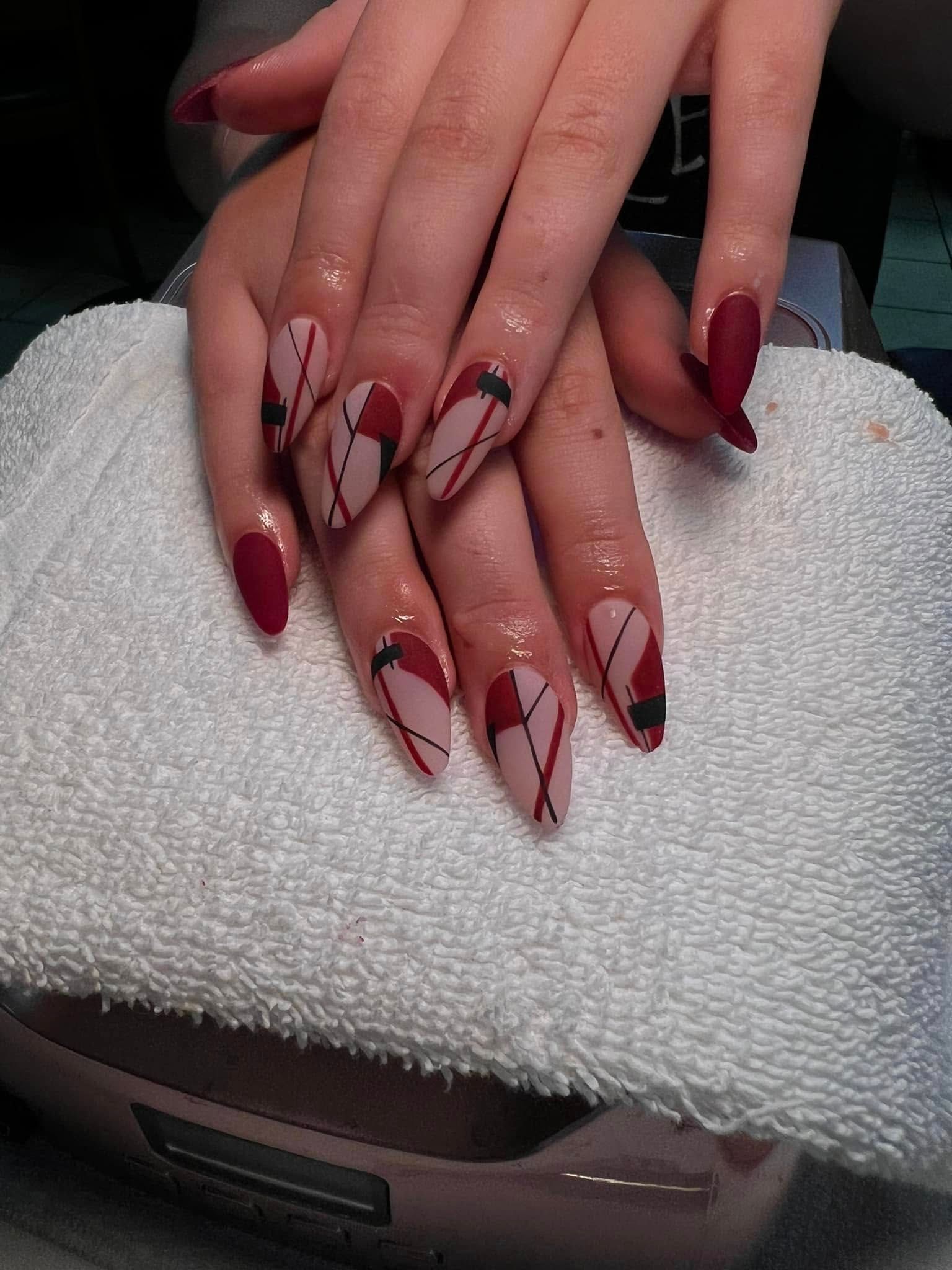 Hands with matte red and neutral nails, abstract black lines, resting on a white towel.