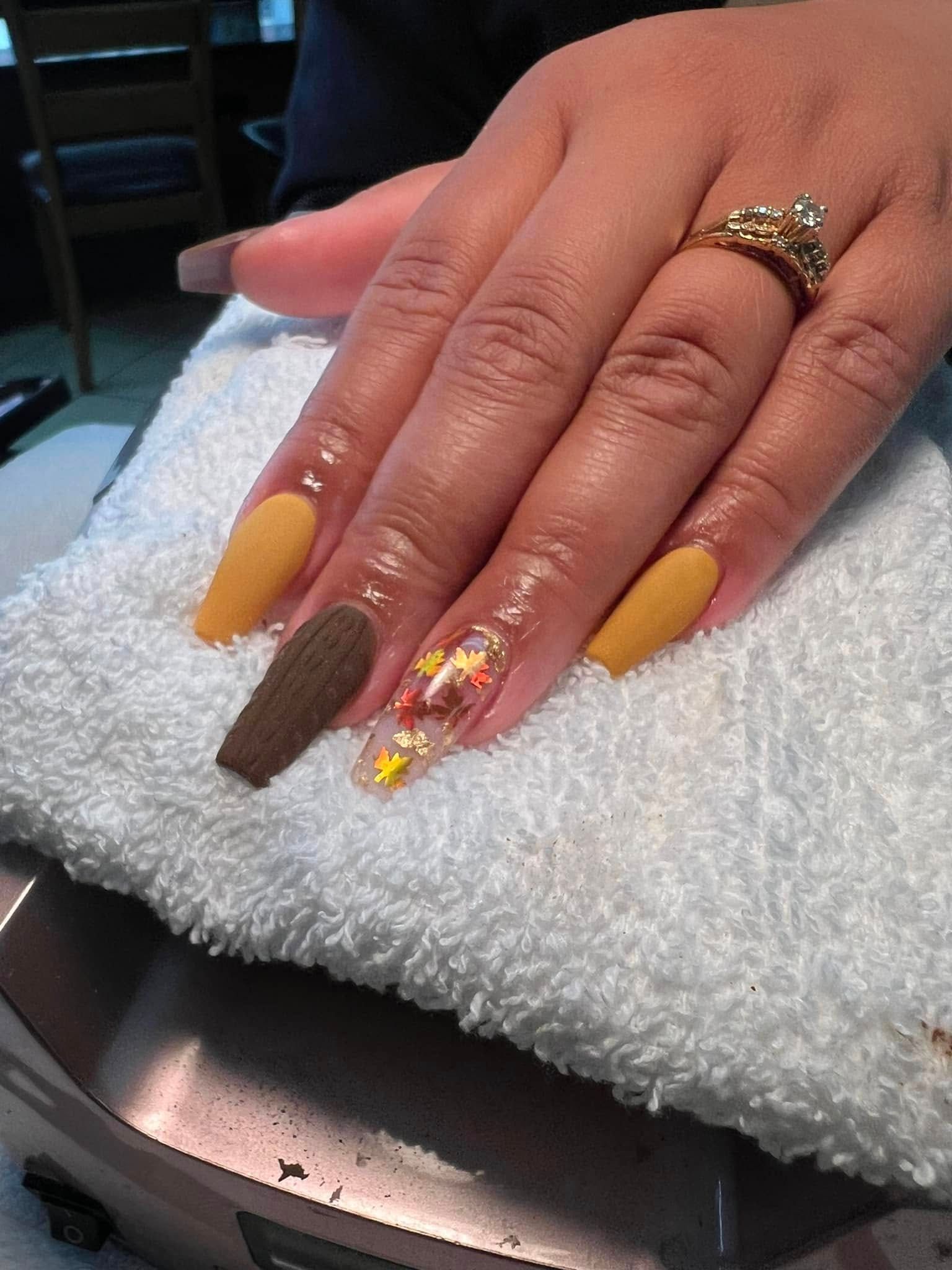 Hand with long, coffin-shaped nails. Colors are brown, mustard, and clear with embedded fall leaf decorations.