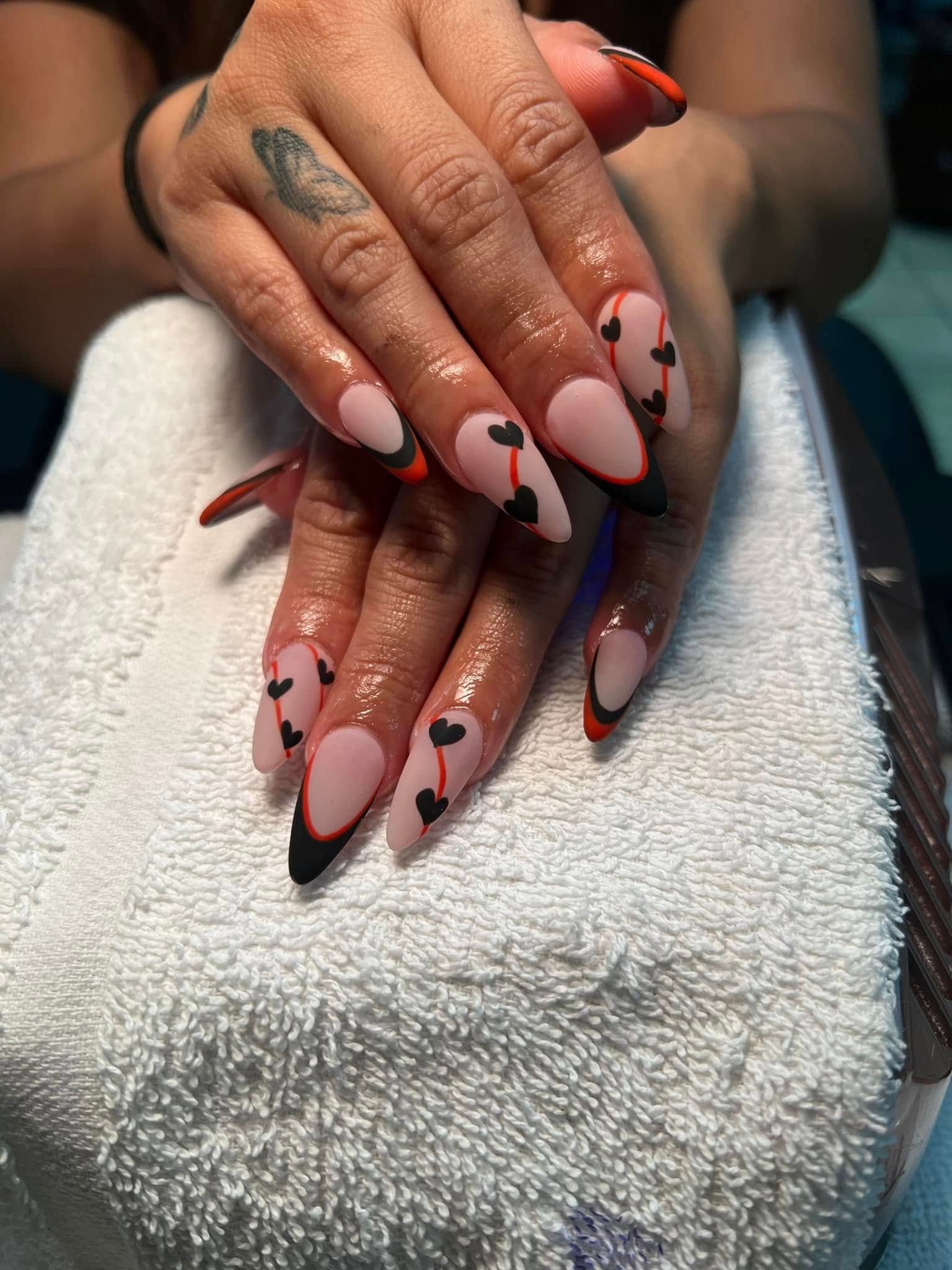 Manicured almond-shaped nails with pink, black, and red heart designs, resting on a white towel.