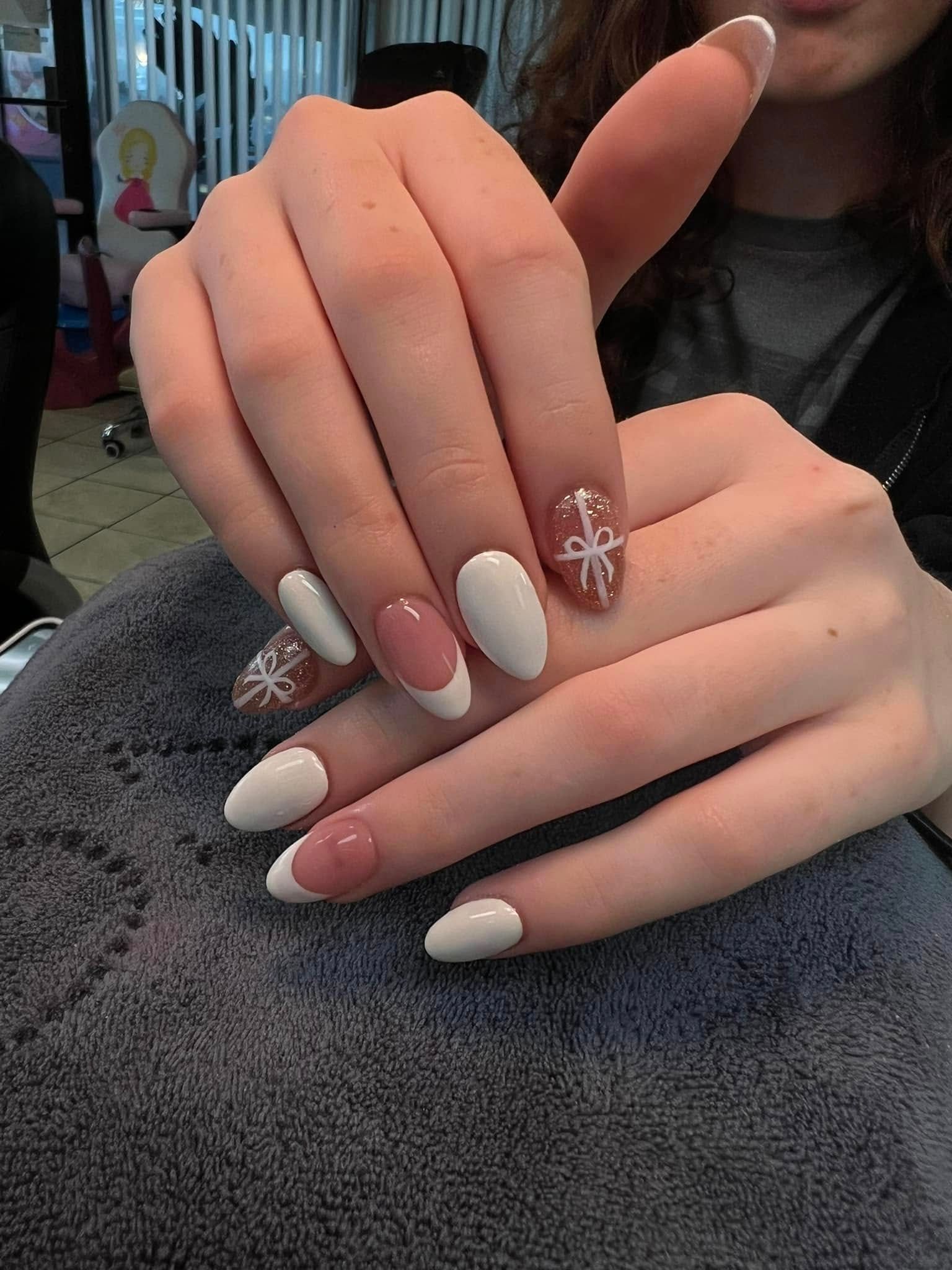 Hands with oval-shaped nails, some white, some pink with snowflake designs. Sitting on a grey towel.