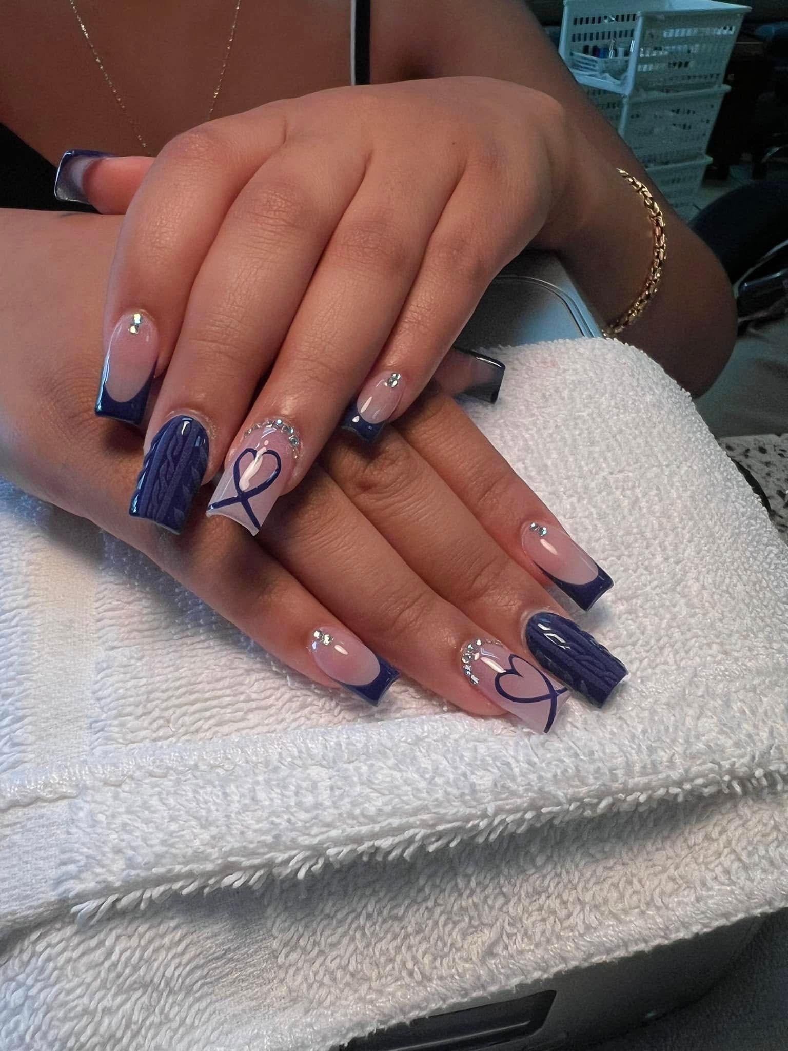 Hands with blue and white French tip nails, some adorned with ribbon and rhinestones, resting on a white towel.