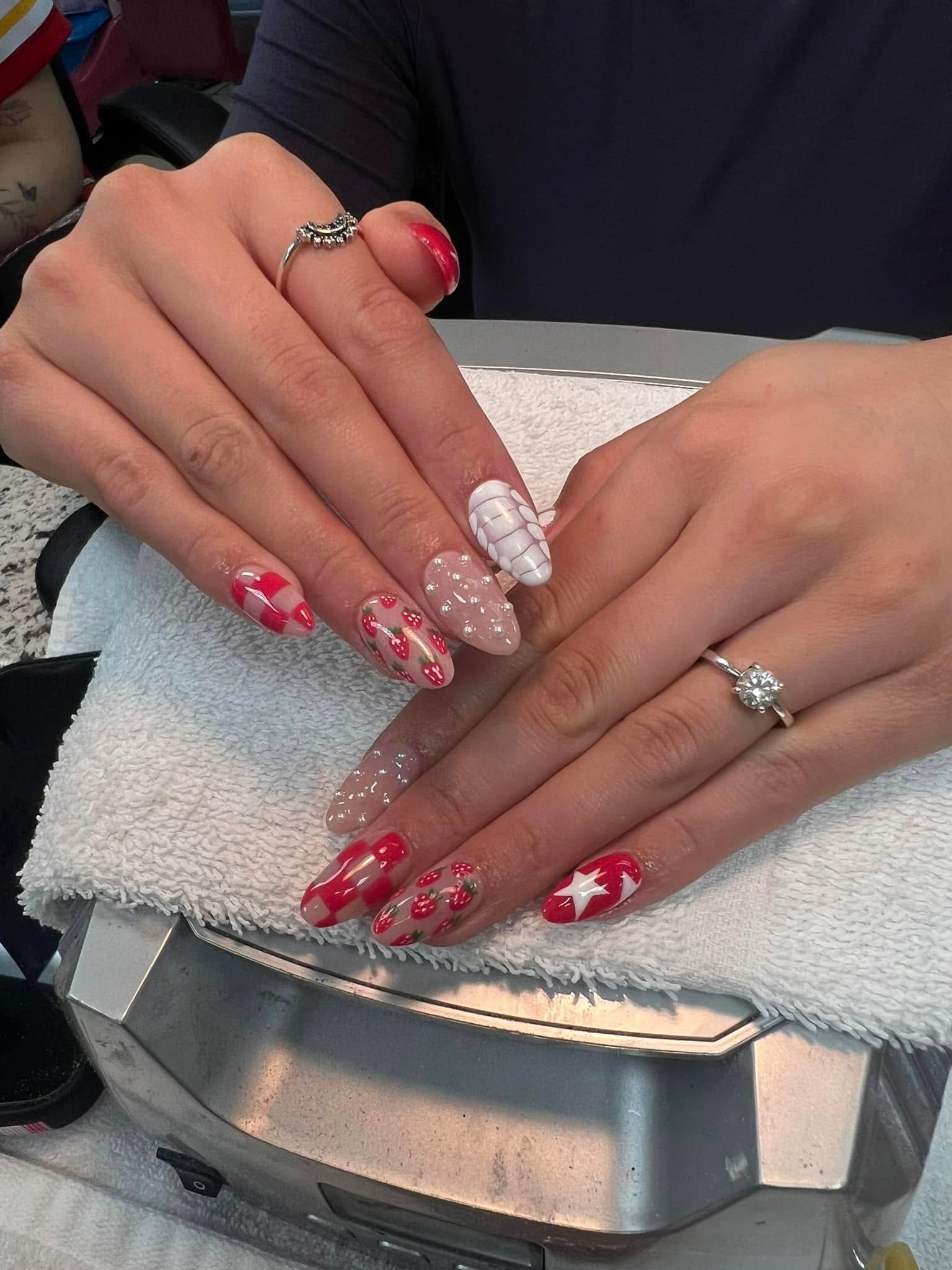 Hands with oval-shaped nails, red and white designs: polka dots, plaid, and stars. Silver rings on fingers.