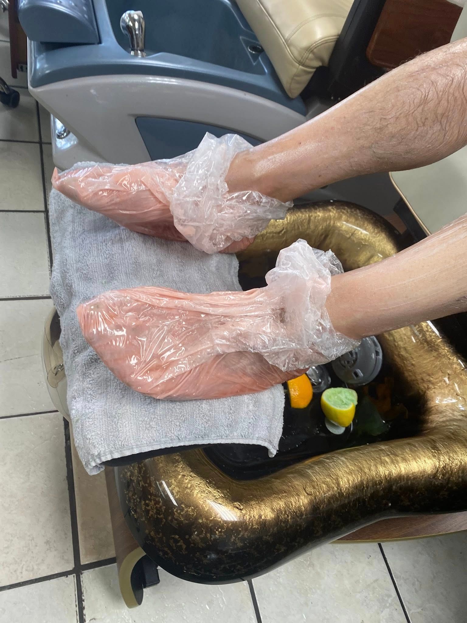 Feet wrapped in plastic sleeves resting on a towel in a pedicure chair.
