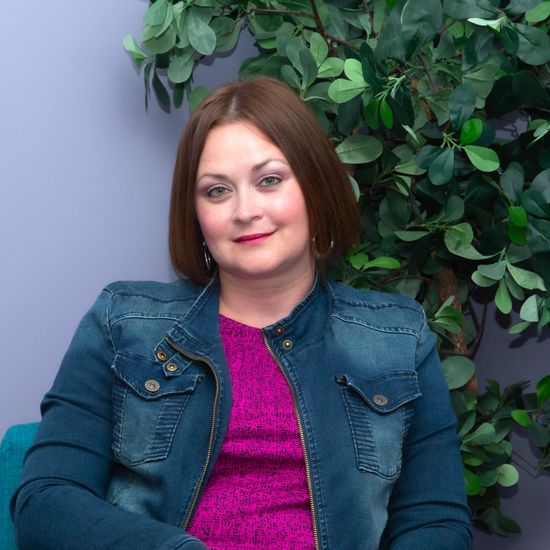 A woman is sitting at a desk with a laptop and a vase of flowers.
